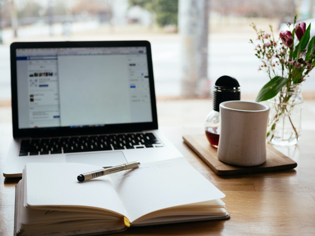 laptop and notepad on a table with a coffee mug and plant