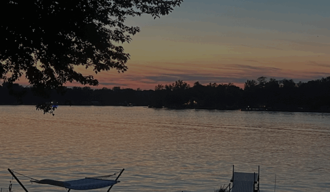 a sunset over a body of water with a hammock in the foreground